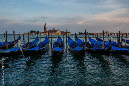 Docked gondola float in the waters near St Mark's Square, with the bell tower of the Church of San Giorgio Maggiore in the background in Venice, Italy at sunset. 