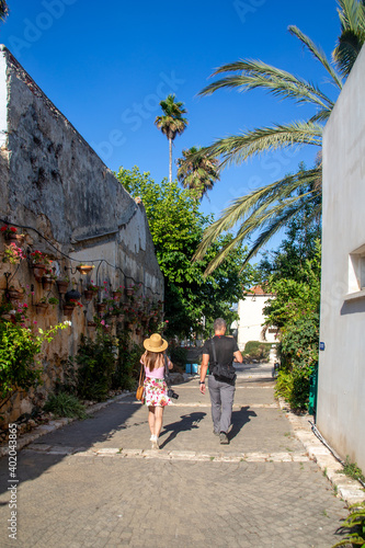 Young woman and man walking down the street by the wall of hanging plant pots with flowers and irrigation systemat the Midrechov Street in Zichron Yaakov Israel photo