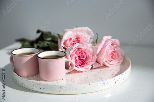 Two small pink cappuccino cups with three pink roses on a tray on a coffee table