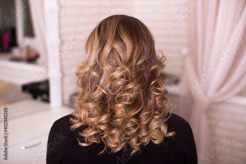 Female back with curly, ombre, brunette hair, in hairdressing salon