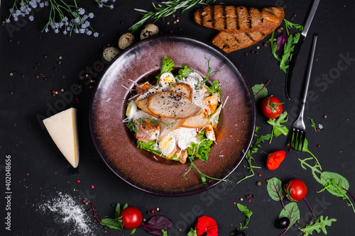 Caesar salad with grilled chicken fillet and slices of bacon, with tomatoes and Caesar sauce. Sprinkled with Parmesan cheese with wheat croutons and quail egg. on a dark background