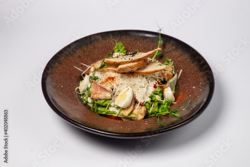 Caesar salad with grilled chicken fillet and slices of bacon, with tomatoes and Caesar sauce. Sprinkled with Parmesan cheese with wheat croutons and quail egg. on a white background