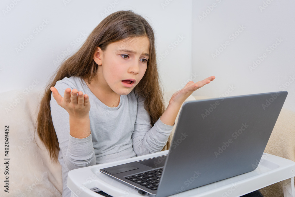 Emotional portrait of attractive cute girl 6-7 old she is tired in a bad mood sitting using laptop on distance learning Emotional portrait of attractive cute girl 6-7 old she is tired in a bad mood sitting using laptop on distance learning