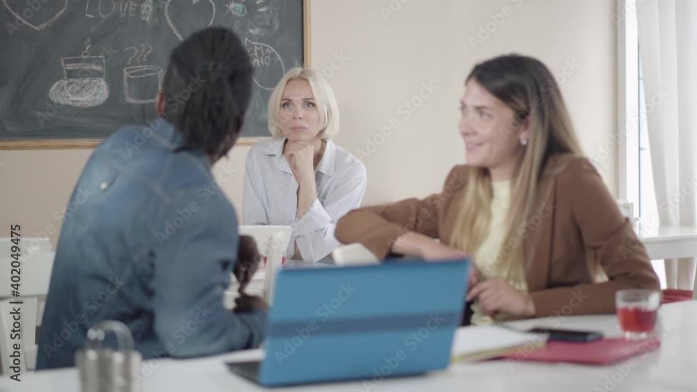 Portrait of gorgeous blond Caucasian woman talking to multiethnic coworkers sitting in lunchroom at front. Positive colleagues chatting during lunch in canteen. Teamwork and friendship concept. Portrait of gorgeous blond Caucasian woman talking to multiethnic coworkers sitting in lunchroom at front. Positive colleagues chatting during lunch in canteen. Teamwork and friendship concept.