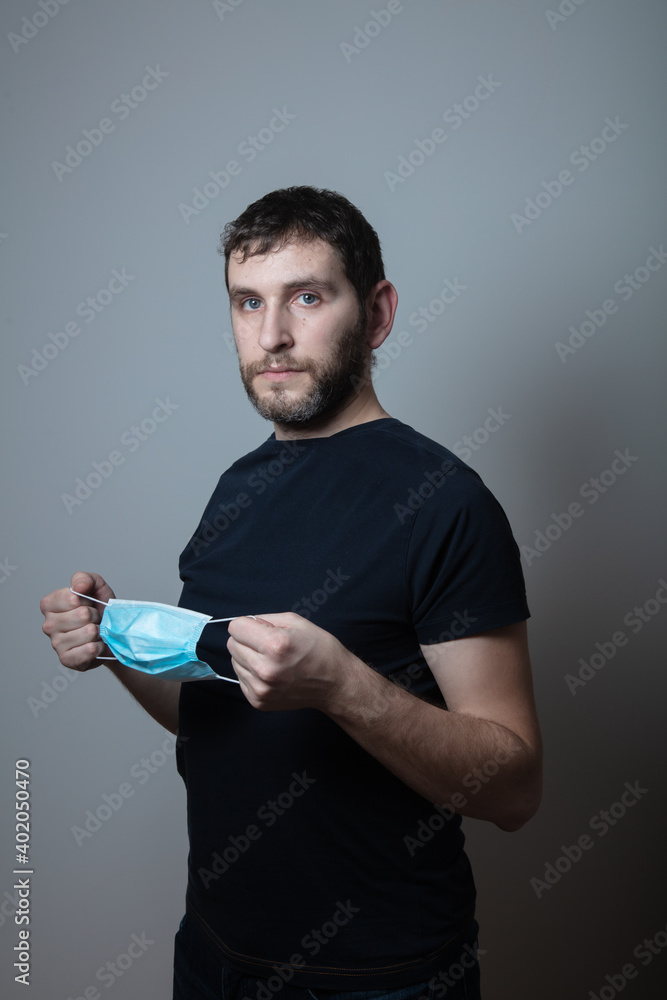 man in black shirt stands stands sideways with a medical mask in his hand on a grey background man in black shirt stands stands sideways with a medical mask in his hand on a grey background