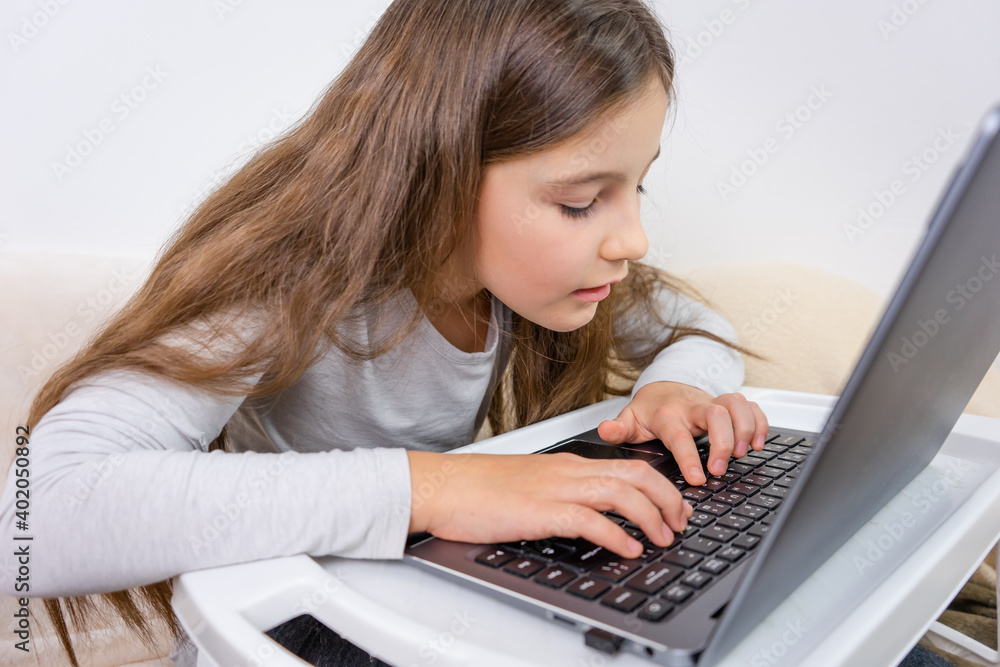 Emotional portrait of attractive cute girl 6-7 old sitting using laptop indoor white background distance learning Emotional portrait of attractive cute girl 6-7 old sitting using laptop indoor white background distance learning