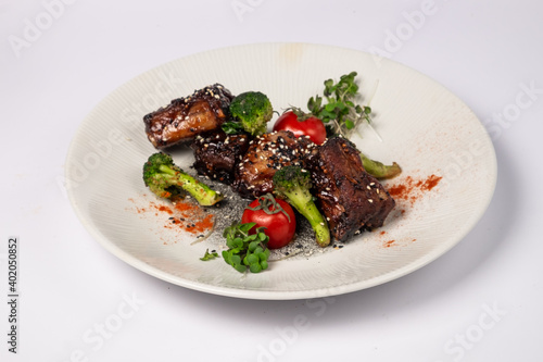 Grilled pork ribs in honey glaze with tomatoes and broccoli on a white background