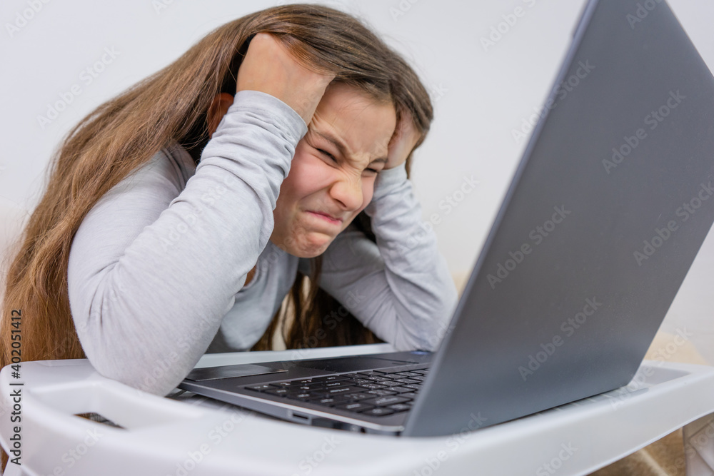 Emotional portrait of attractive cute girl 6-7 old she is tired in a bad mood sitting using laptop on distance learning Emotional portrait of attractive cute girl 6-7 old she is tired in a bad mood sitting using laptop on distance learning