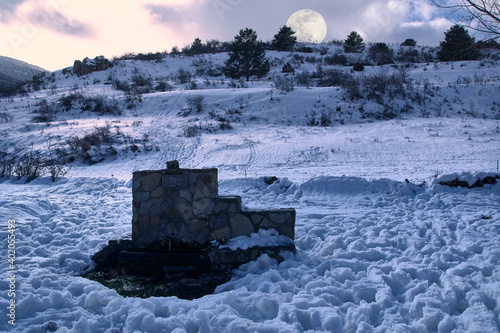 Water fountain in the snow with the full moon