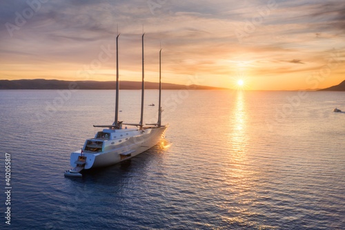 Aerial view of luxury yacht in blue sea at sunset in summer. Big modern sail boat. Top view of beautiful futuristic yacht, water, reflection, mountain, colorful sky with clouds. Travel in Adriatic sea © den-belitsky