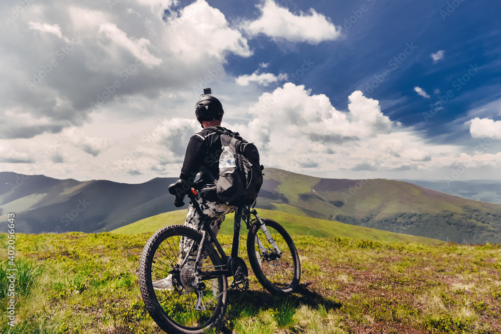 A young guy stands with a bicycle on top of a mountain