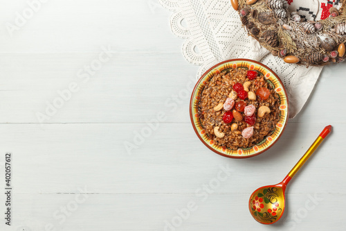 Kutya, a porridge of spelt with nuts,Candied fruits, honey and Chia. On a light wooden background, with a painted wooden spoon on a linen napkin.top view, space