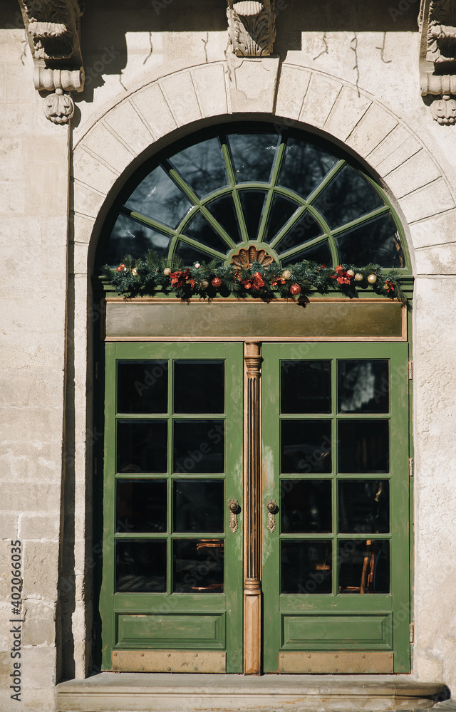 Obraz premium The doorway of the old Baroque style with a complex design with green wooden door. Christmas tree decoration on New Year's Eve. The facade of the building in Lviv, Ukraine.