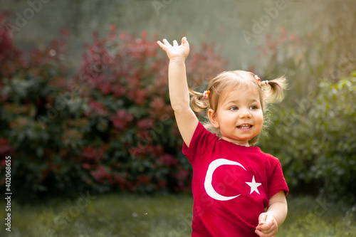 Portrait of happy little kid, cute baby toddler with Turkish flag t-shirt wave her hand. Patriotic holiday. Adorable child celebrates national holidays. Blur background with copy space for text.