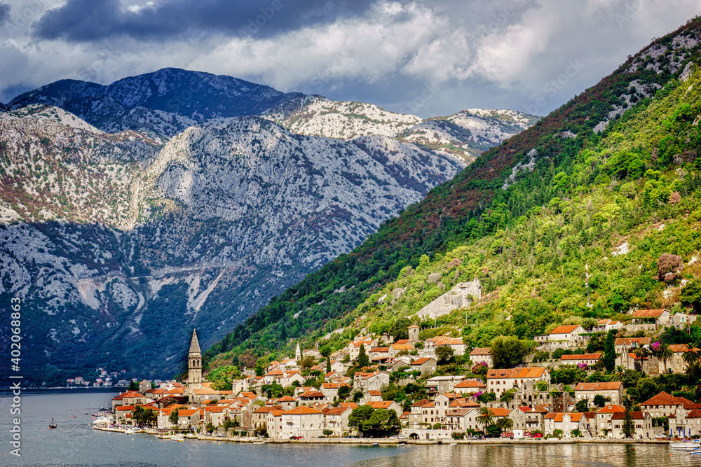 A serene city with a church steeple in the distance, Kotor Montenegro, sits on the edge of the bay surrounded by towering mountains A serene city with a church steeple in the distance, Kotor Montenegro, sits on the edge of the bay surrounded by towering mountains