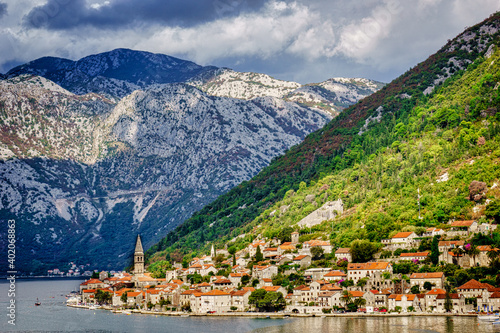 A serene city with a church steeple in the distance, Kotor Montenegro, sits on the edge of the bay surrounded by towering mountains 