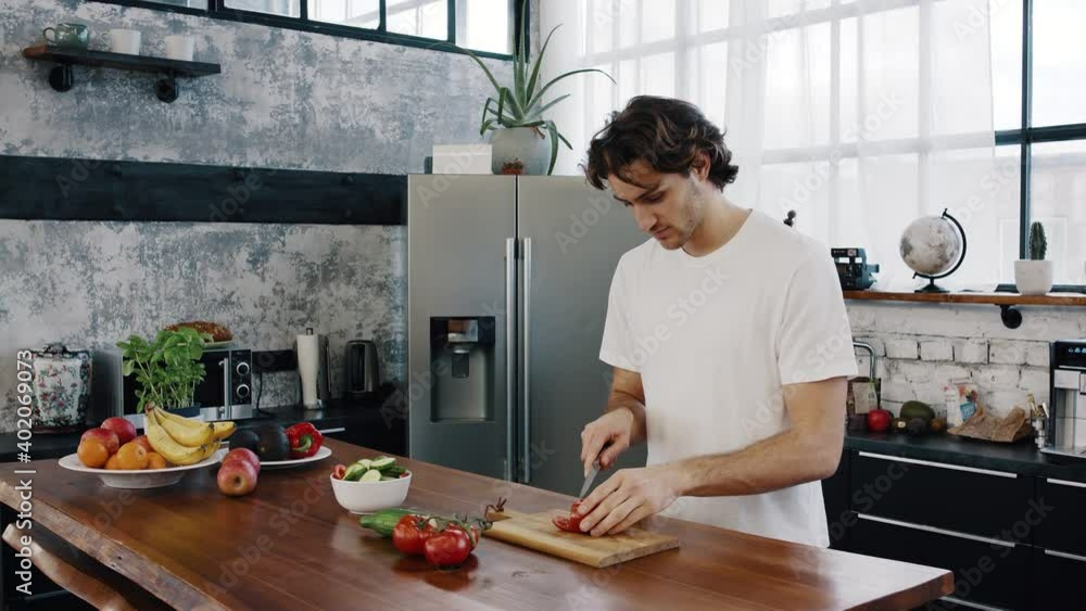 Attractive young man cuts a tomato vegetables and prepares a healthy salat or meal in modern kitchen Attractive young man cuts a tomato vegetables and prepares a healthy salat or meal in modern kitchen