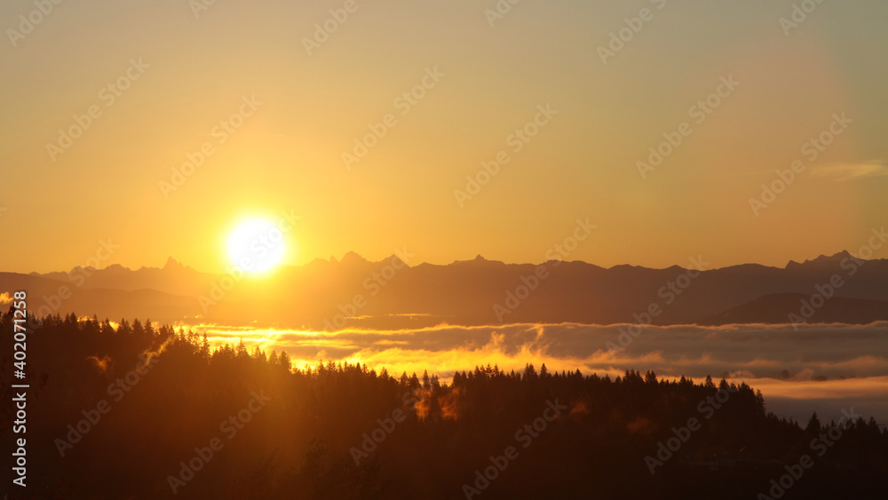Bright sun over low clouds over mountain ridges