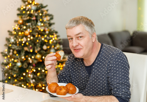 Wallpaper Mural Caucasian man eating olibol near the Christmas tree at home, portret,Oliebollen - Dutch traditional Dessert - Also known as Dutch Doughnuts or dutchies. Torontodigital.ca