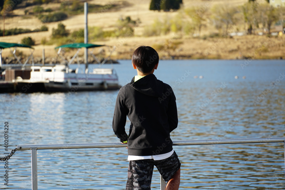 Young sporty Asian boy looking at the view on a wood pier at the Lake. Teenager concept