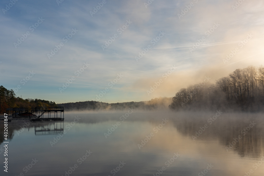 Fog rises by a dock on the surface of the water at sunrise in winter on Lake Lanier in Georgia, USA