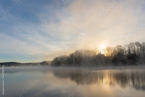 Fog rises on the water of Lake Lanier in Georgia at sunrise under a blue and orange sky