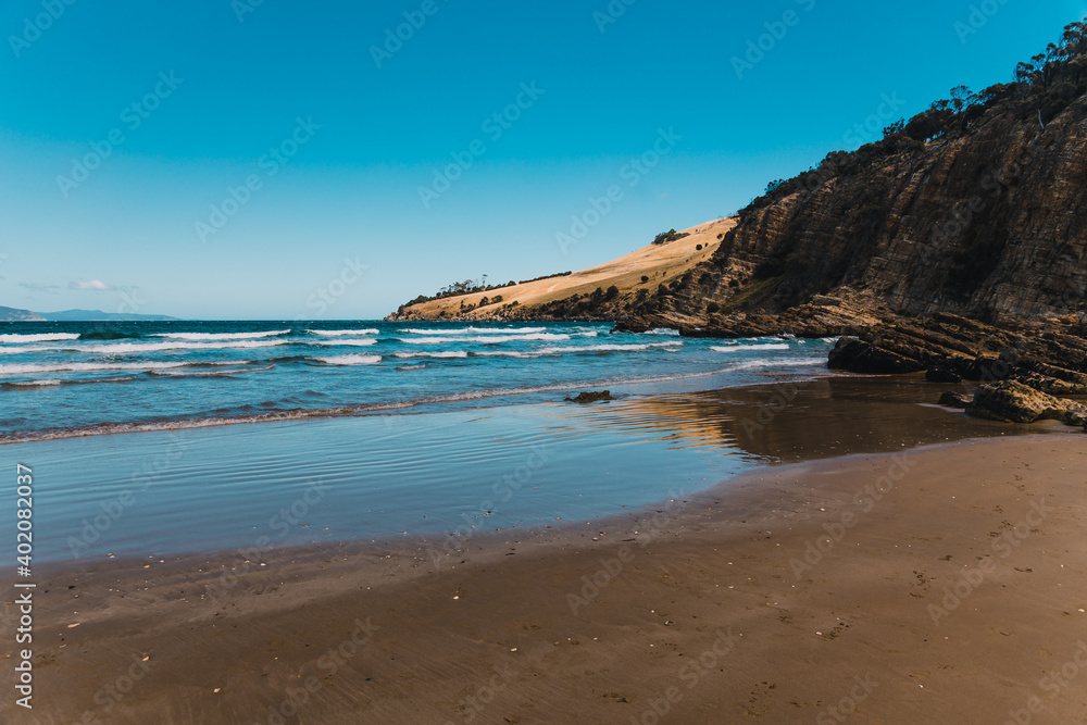 pristine wild landscape at Clifton Beach in Tasmania, Australia with wavy blue ocean and golden sand next to a rugged coastline