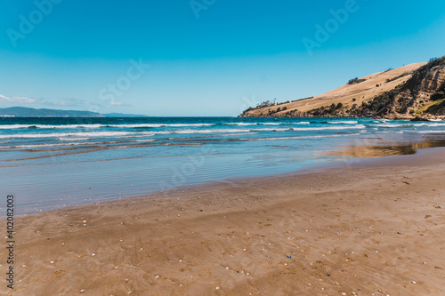 pristine wild landscape at Clifton Beach in Tasmania, Australia with wavy blue ocean and golden sand next to a rugged coastline