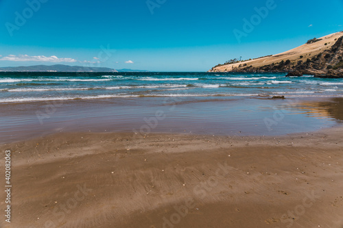 pristine wild landscape at Clifton Beach in Tasmania, Australia with wavy blue ocean and golden sand next to a rugged coastline