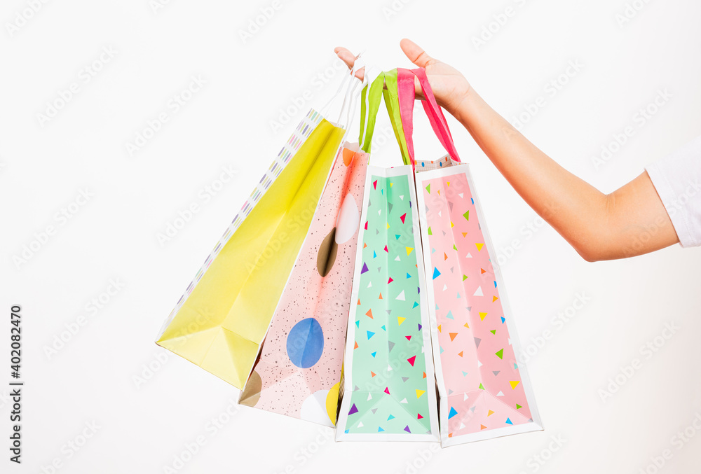 Closeup women hand holding colorful multicolor shopping bag many packets isolated on white background, female holds in hand white clear empty blank craft paper gift bag, shopping day concept
