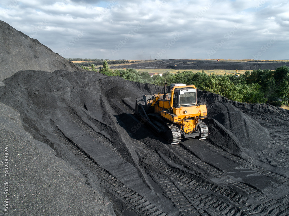 Bulldozer is pushing hard coal. Large coal heap.