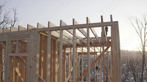 Aerial ascending view of a builder working on the second floor of the frame house under construction. Winter photo