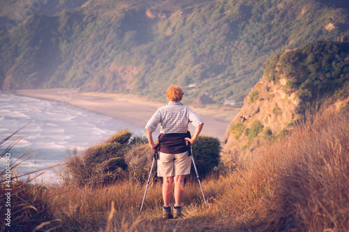 View of older woman hiker looking at North Piha Beach from elevated lookout in evening light photo