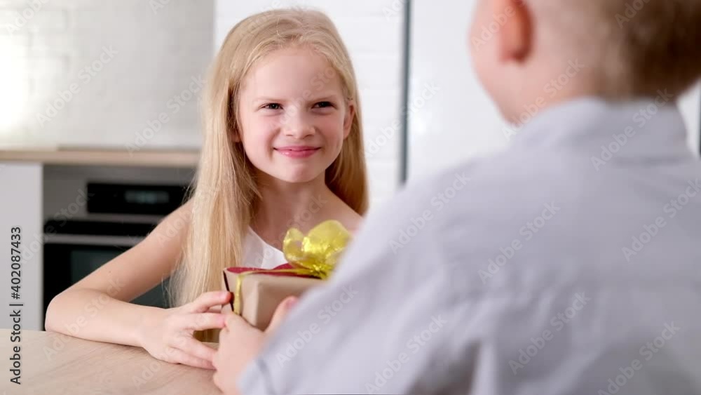 Little boy gives his beloved girl Valentines Day gift box. Happy smiling blonde kids celebrating Valentines day. Slow motion Little boy gives his beloved girl Valentines Day gift box. Happy smiling blonde kids celebrating Valentines day. Slow motion