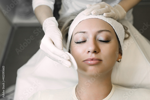 beautician cleans the patient s skin with a cotton pad