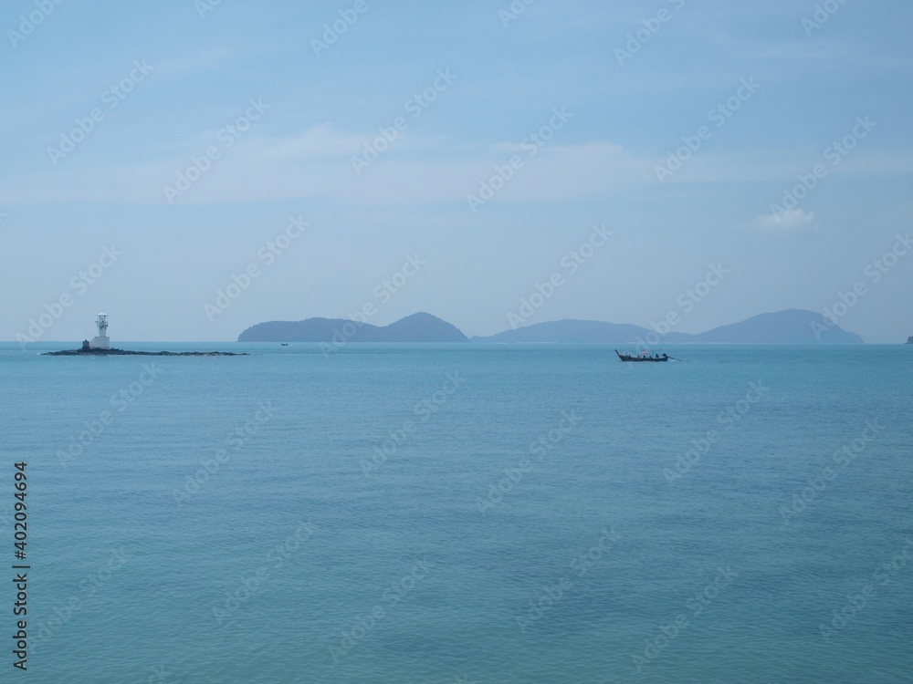 Seascape. Panorama of sea, boat, islands and a lighthouse. Lighthouse on a rocky island. Longtail boat with tourists rushes along the surface of the sea. Thailand. Tropical vacation. Popular resort