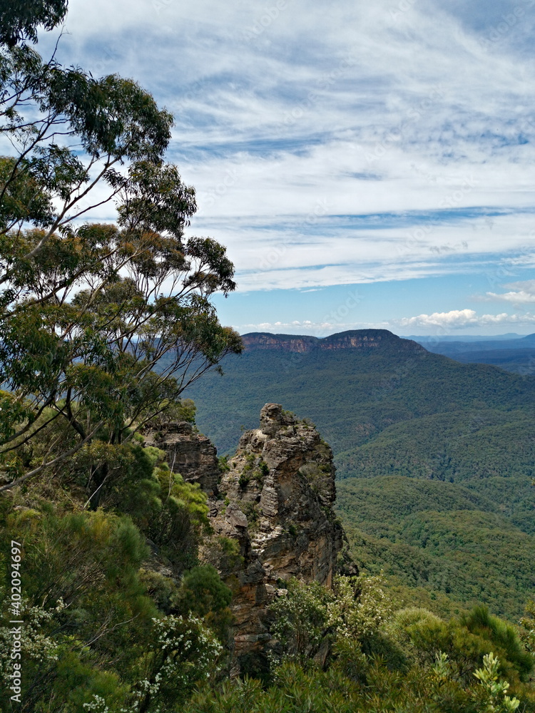Beautiful view of tall mountain peak, with mountains, valleys, trees, blue sky and white clouds in the background ,Three Sisters Lookout, Blue Mountain National Park, New South Wales, Australia
