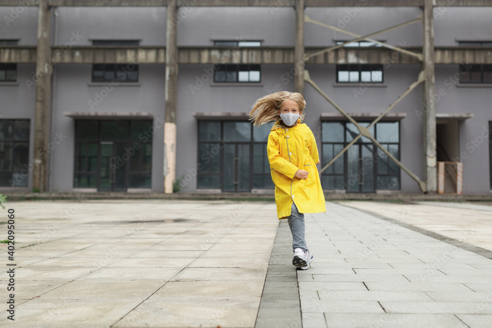 little caucasian girl 7 years old with blonde hair in yellow raincoat and face mask during Coronavirus pandemic. Colors of the year 2021 ultimate gray and illuminating
