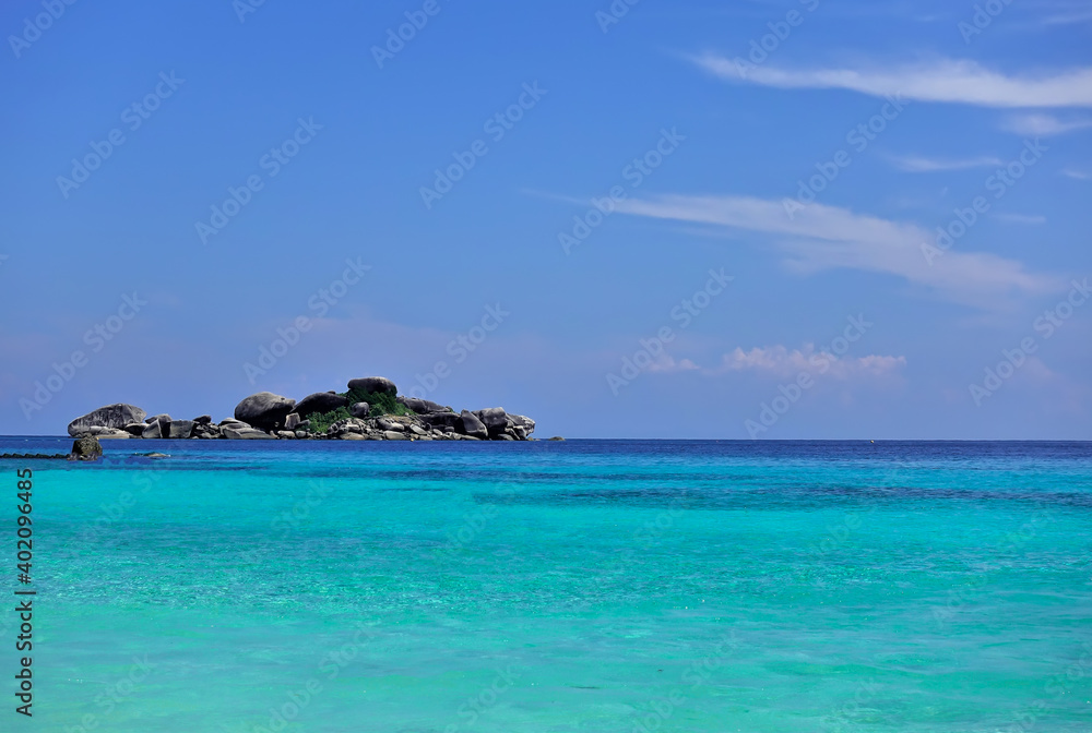 The clear aquamarine water of the Andaman Sea is calm. A small island with picturesque boulders is visible on the horizon. Cirrus clouds in the azure sky. Thailand. Similan islands