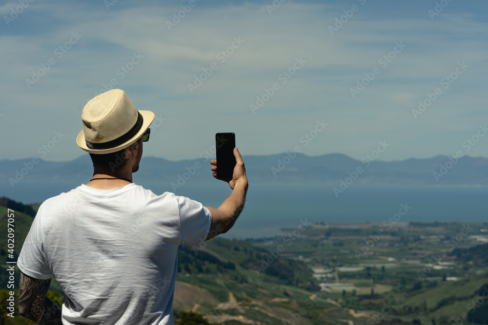 Obraz premium Young man taking a selfie with smartphone at Takaka Hill, Hawkes Lookout. New Zealand