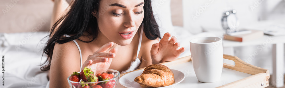  brunette woman having croissant, strawberry and cocoa for breakfast in bed, banner