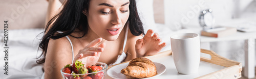  brunette woman having croissant, strawberry and cocoa for breakfast in bed, banner