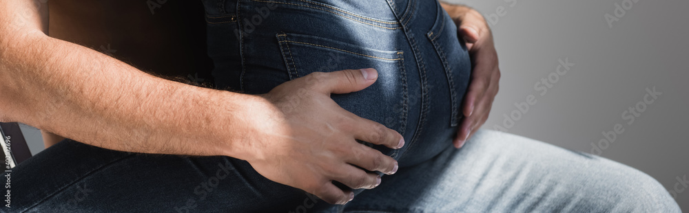 Cropped view of man touching buttocks of girlfriend in jeans isolated on grey, banner Cropped view of man touching buttocks of girlfriend in jeans isolated on grey, banner