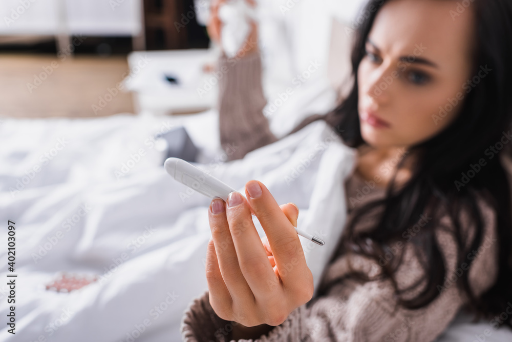 blurred ill young woman in sweater lying in bed with thermometer and tissue blurred ill young woman in sweater lying in bed with thermometer and tissue