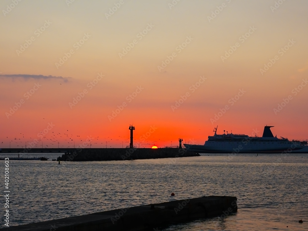 The ship enters the sea bay against the backdrop of the setting sun and birds circling over the sea