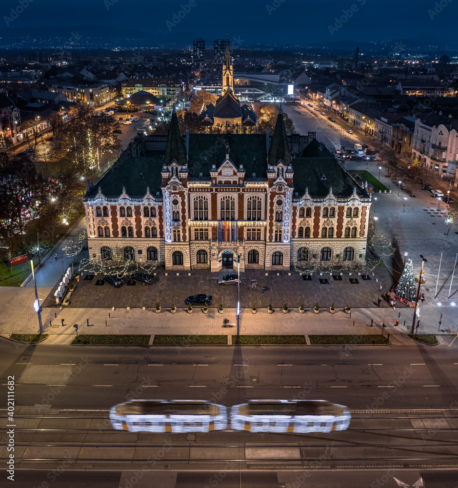 Budapest, Hungary - Aerial panoramic view of Ujpest city centre with City Hall building, St. Stephen's square and church, Christmas tree and light tram on the move taken on a December evening