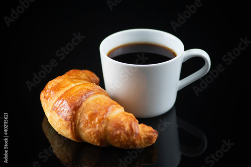 Croissant and White Cup of Coffee on Black Reflective Background