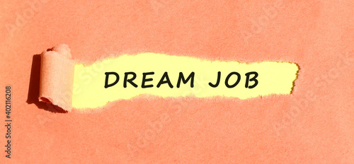 The text DREAM JOB appearing on yellow paper behind torn color paper. Top view.