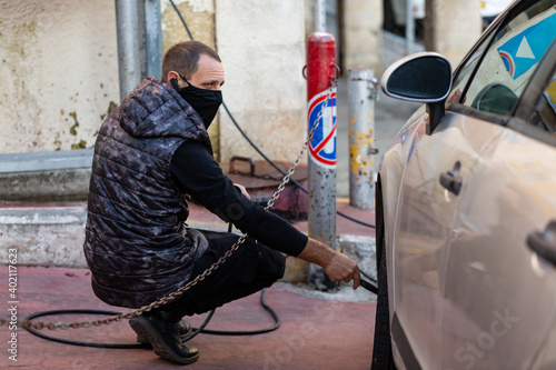Masked car mechanic shakes a car wheel on the street in service station, automatic pump, auto tire pumping. Car mechanic inflating tire