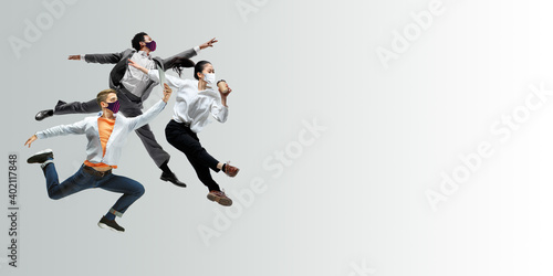 Happy office workers in face masks jumping and dancing in casual clothes or suit isolated on studio background. Business  start-up  prevention of COVID  motion and action concept. Creative collage.